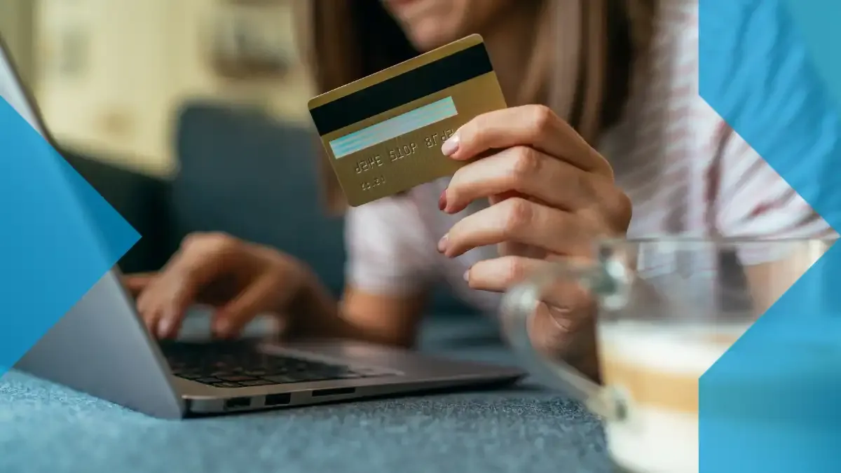 Personne tenant une carte bancaire tout en utilisant un ordinateur portable, représentant l’aspect numérique des paiements transfrontaliers et des transferts d’argent en ligne.