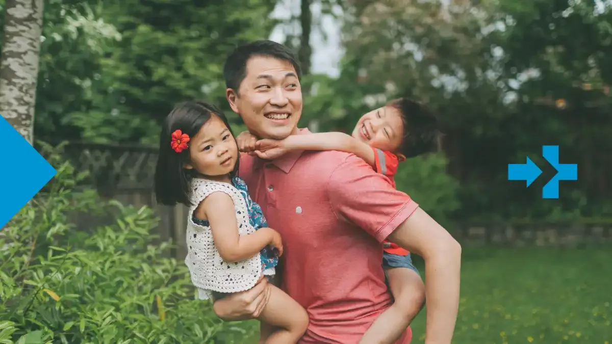 Padre sonriente sostiene a sus dos hijos pequeños al aire libre en un jardín, celebrando juntos el Día del Padre.