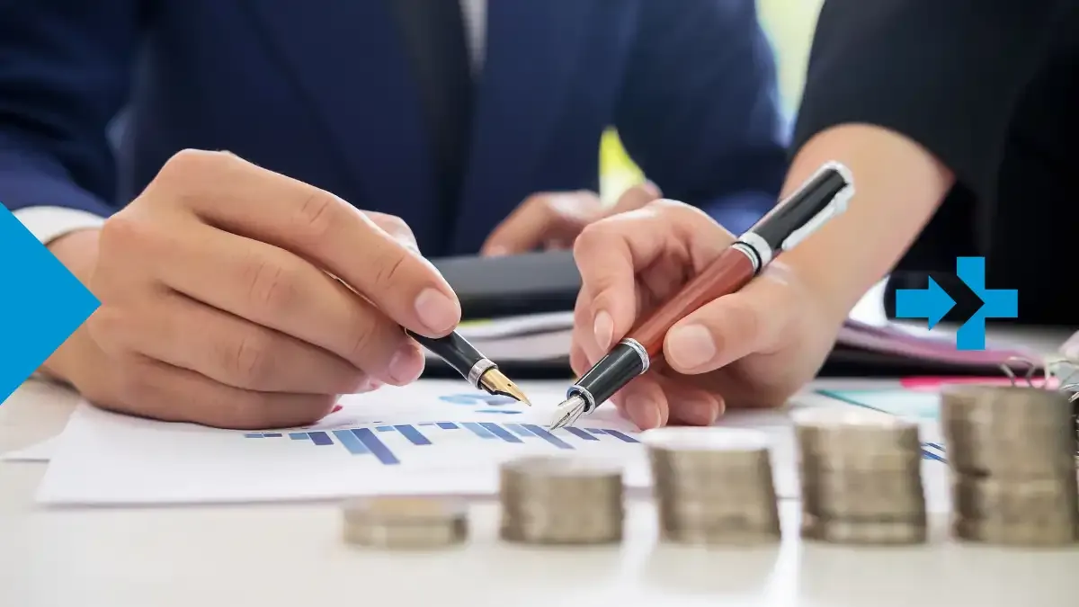 Two professionals analyzing financial data with pens, charts, and stacked coins on the table.