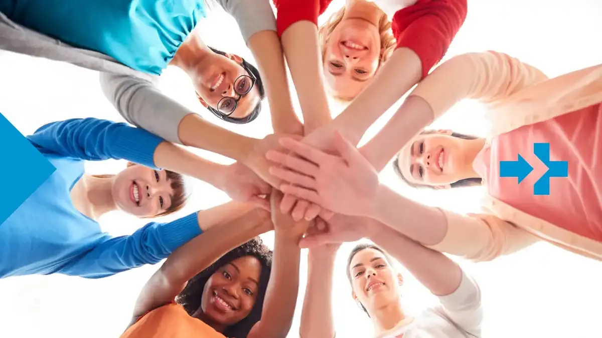 A diverse group of smiling friends standing in a circle with their hands stacked together in unity, symbolizing global friendship and connection.