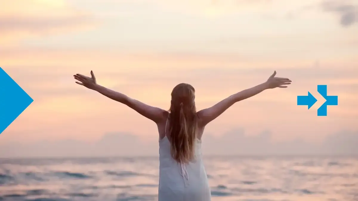Mujer frente al mar con los brazos abiertos al amanecer, símbolo de libertad y orgullo.