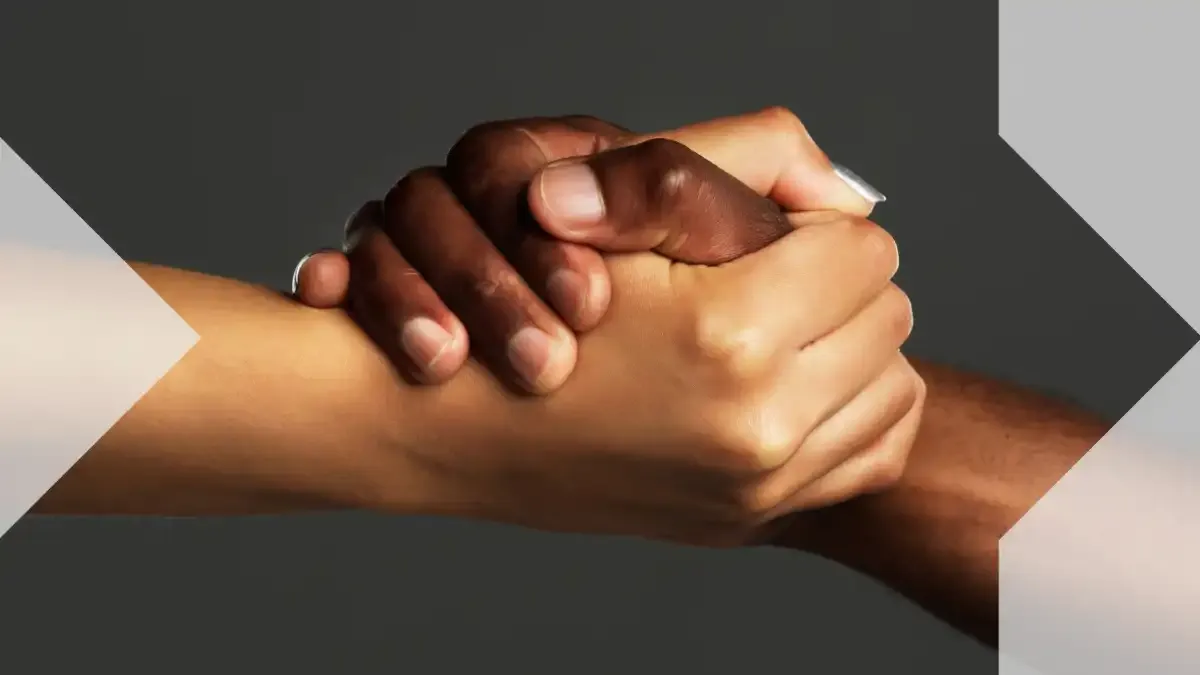 Two people with different skin tones clasp hands, symbolizing family support, connection and help across distances.
